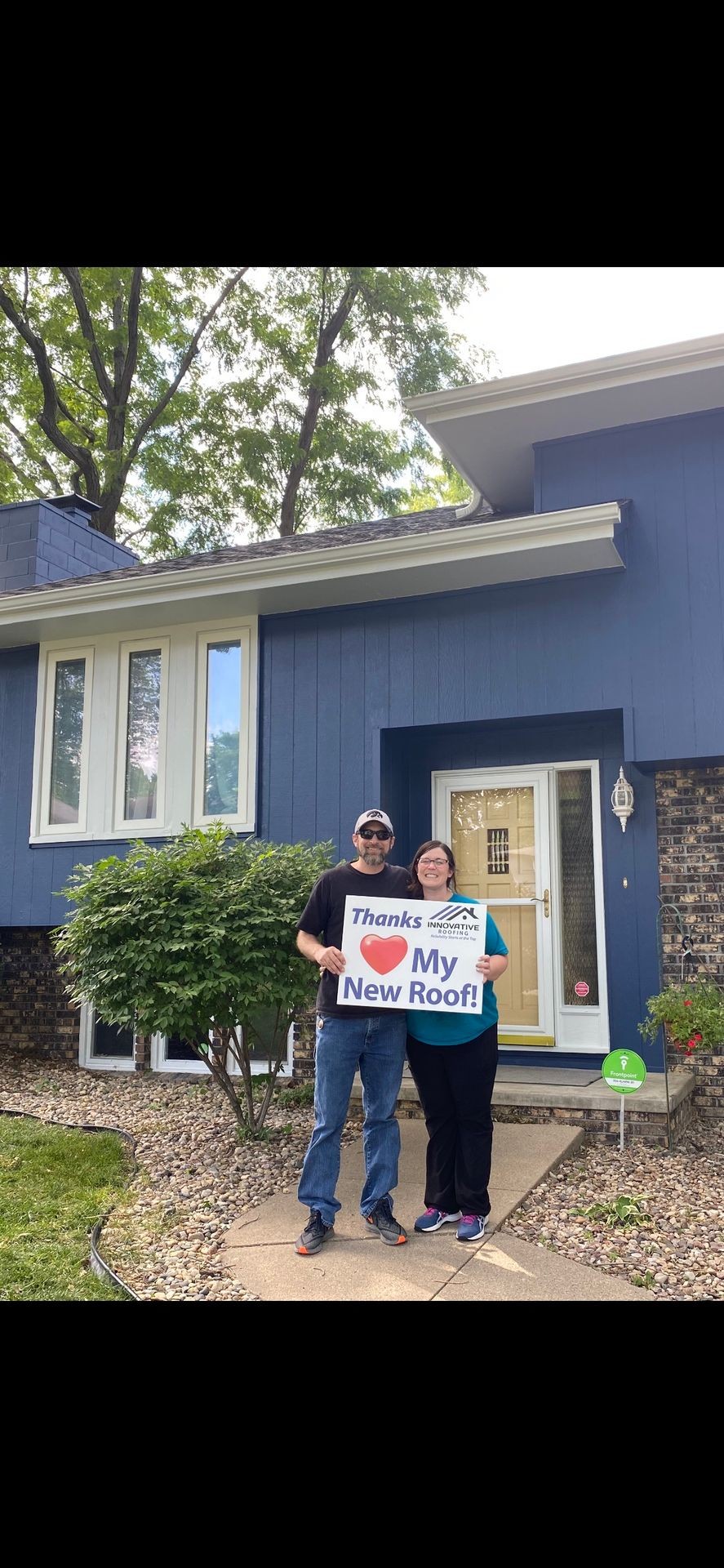 Couple standing outside their house holding a sign thanking for a new roof installation.