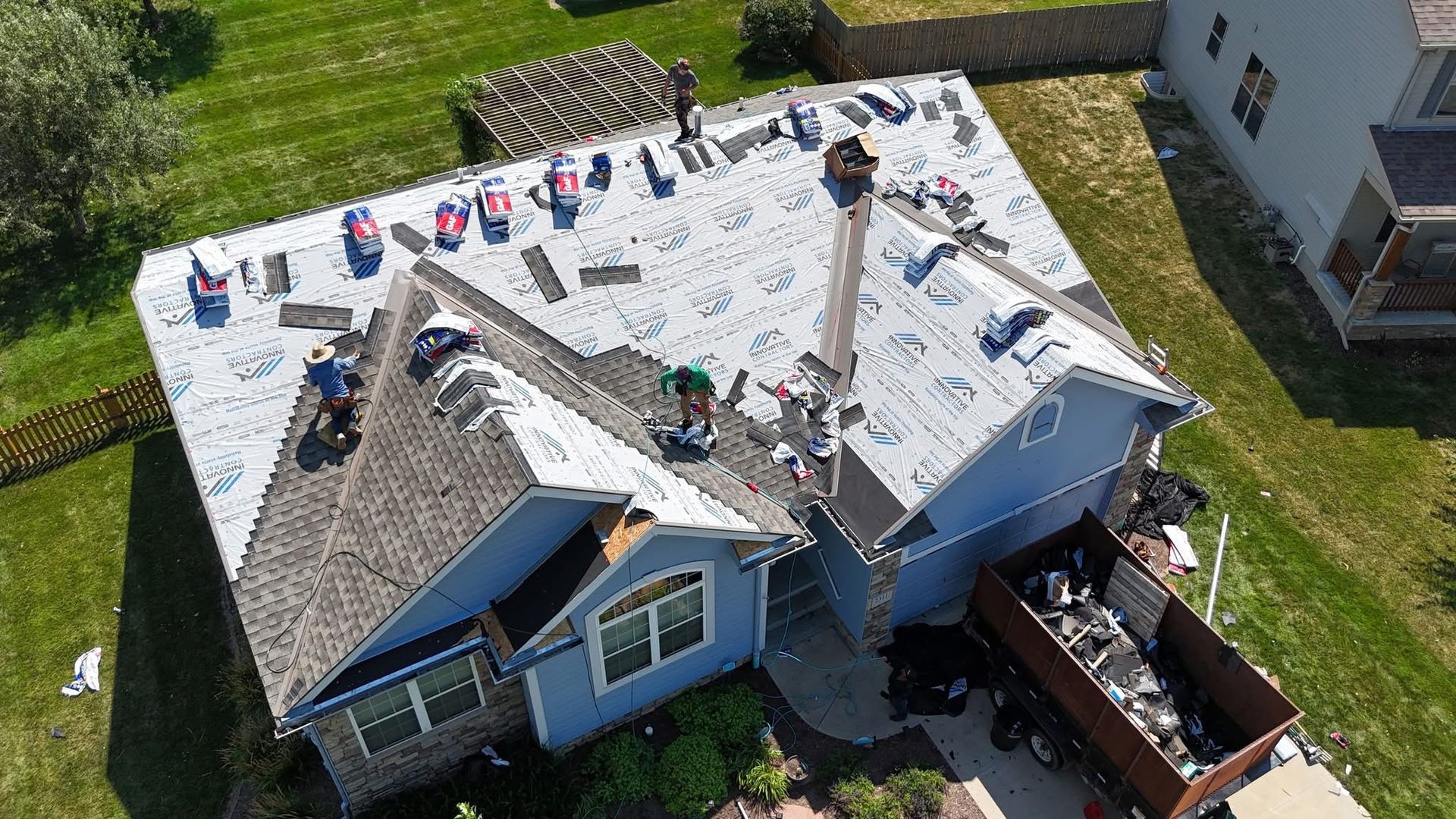 Aerial view of a residential roof under construction with workers installing roofing materials on a sunny day.