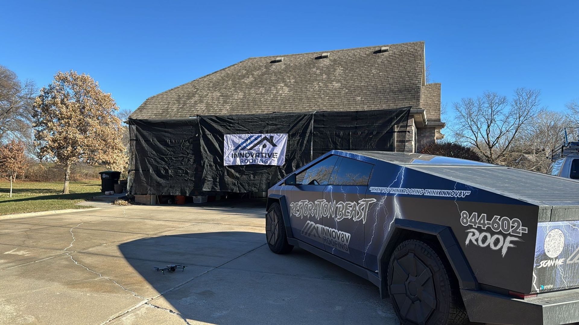 House under renovation with a black tarp, innovative roofing banner, and futuristic vehicle parked outside.